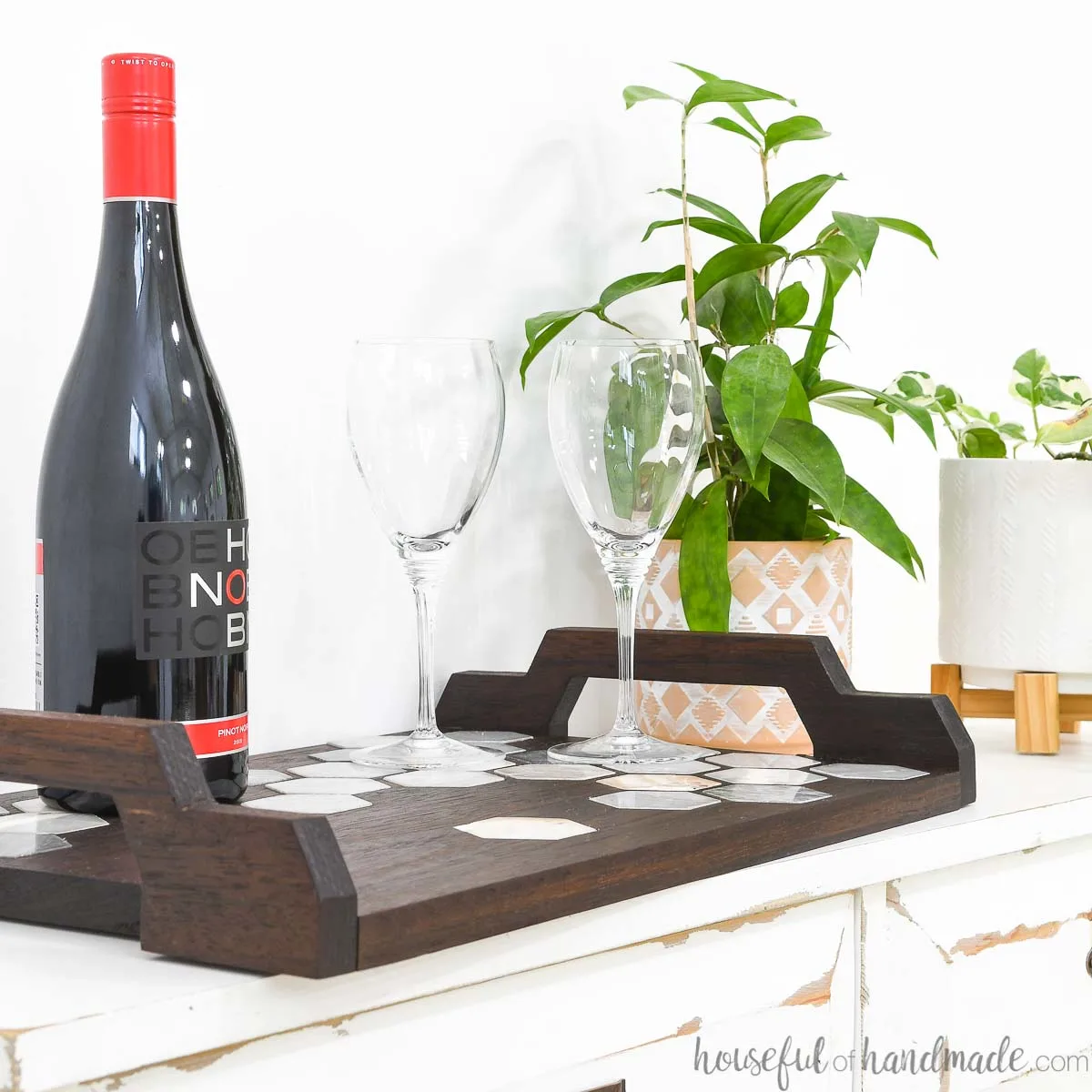Marble hexagon tile inlay tray on a table with wine and glasses on it and plants in the background.