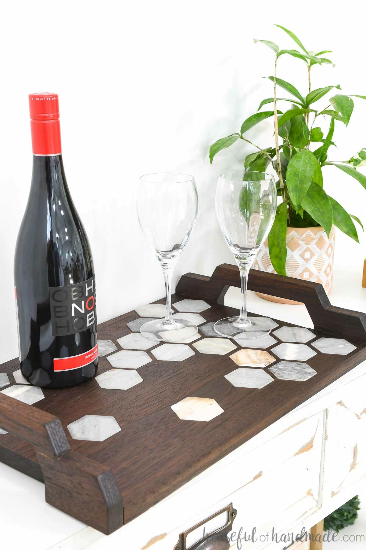 DIY walnut serving tray with marble tile inlay and handles with wine and glasses on top of it. 