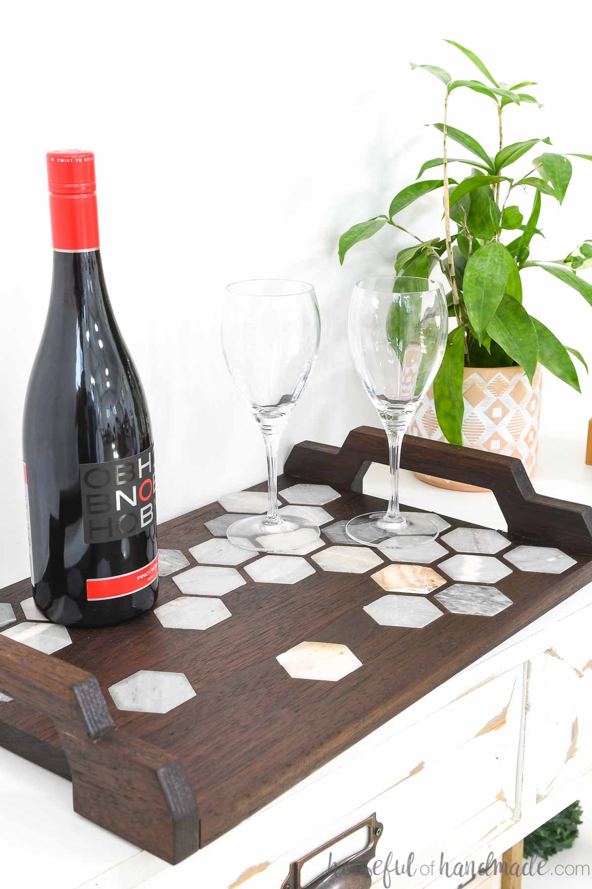 DIY walnut serving tray with marble tile inlay and handles with wine and glasses on top of it.