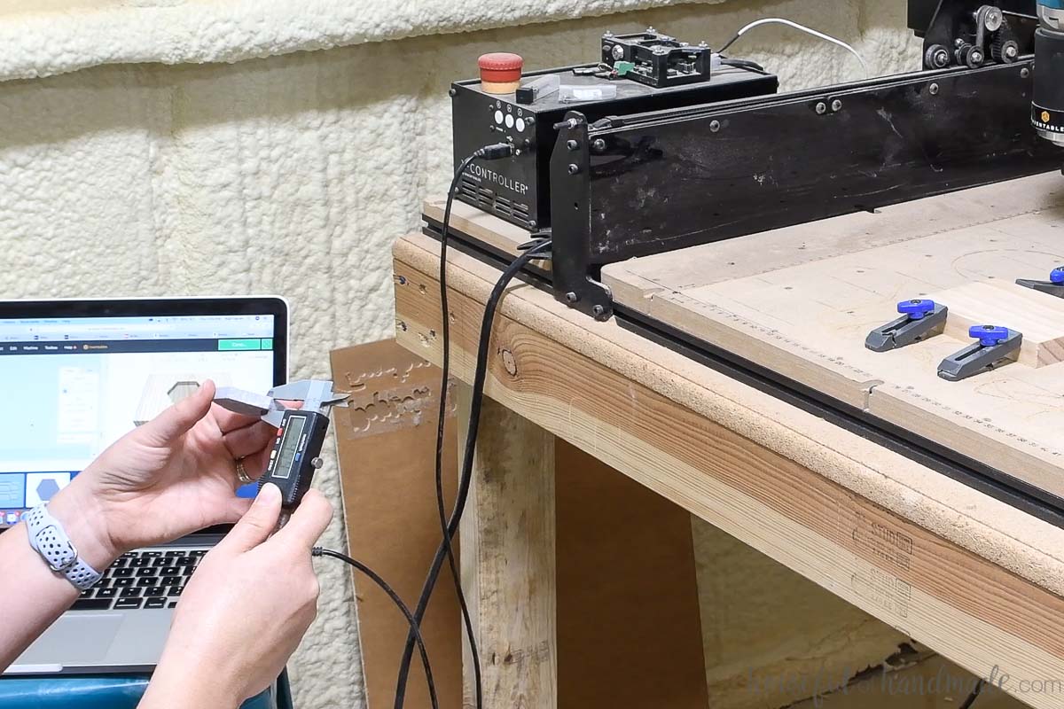 Measuring the thickness of the hexagon marble tile with digital calipers with the CNC machine in the background. 