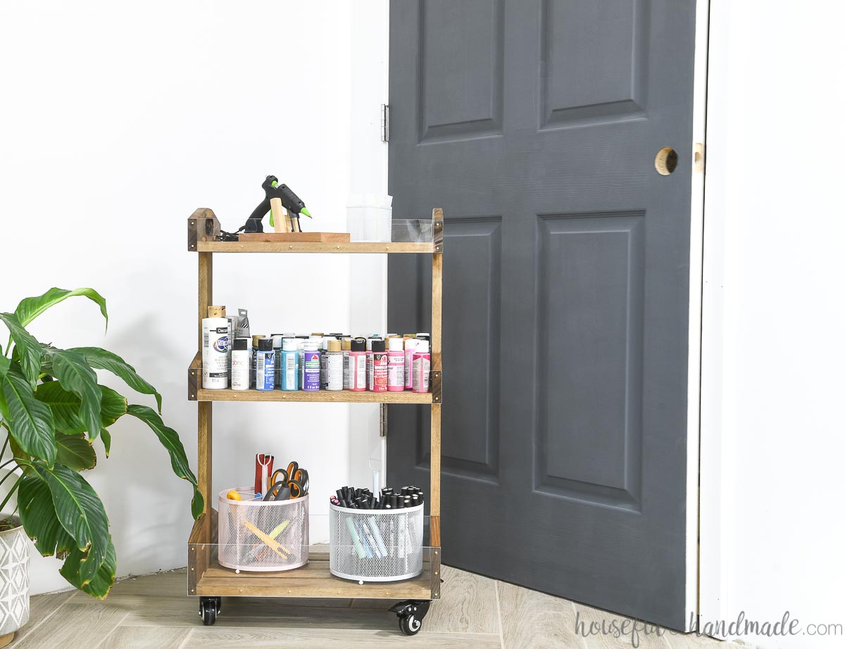 Wood rolling cart loaded with craft supplies in front of a charcoal painted door. 