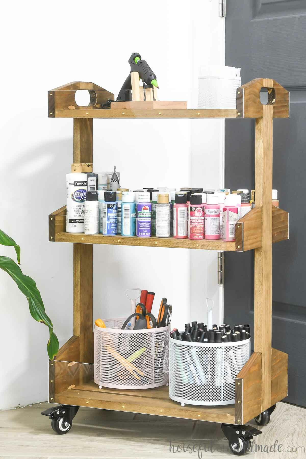 Close up of the easy to build wood rolling cart with craft paint and a glue gun stored in it. 