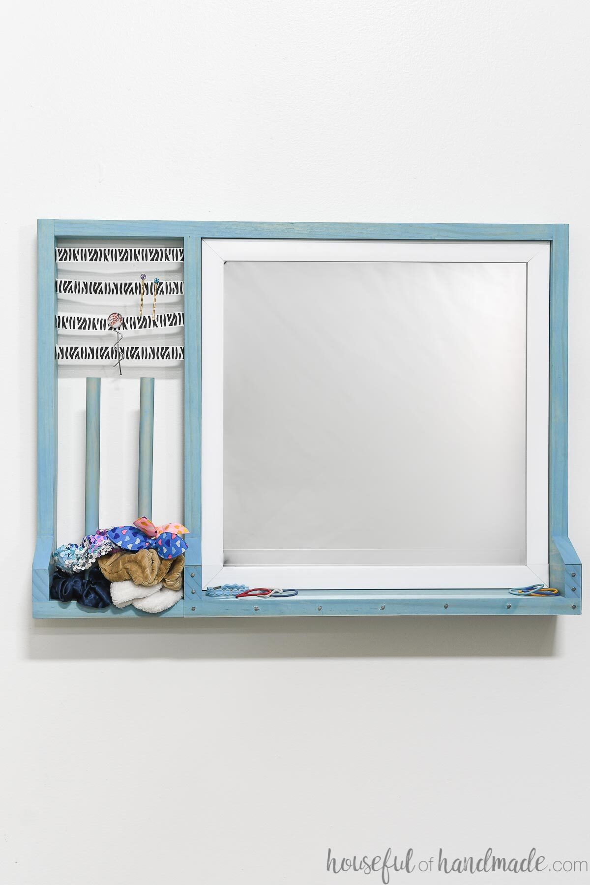 Wall mounted hair accessory organizer with a mirror and storage for scrunchies, hair clips and hair ties. 