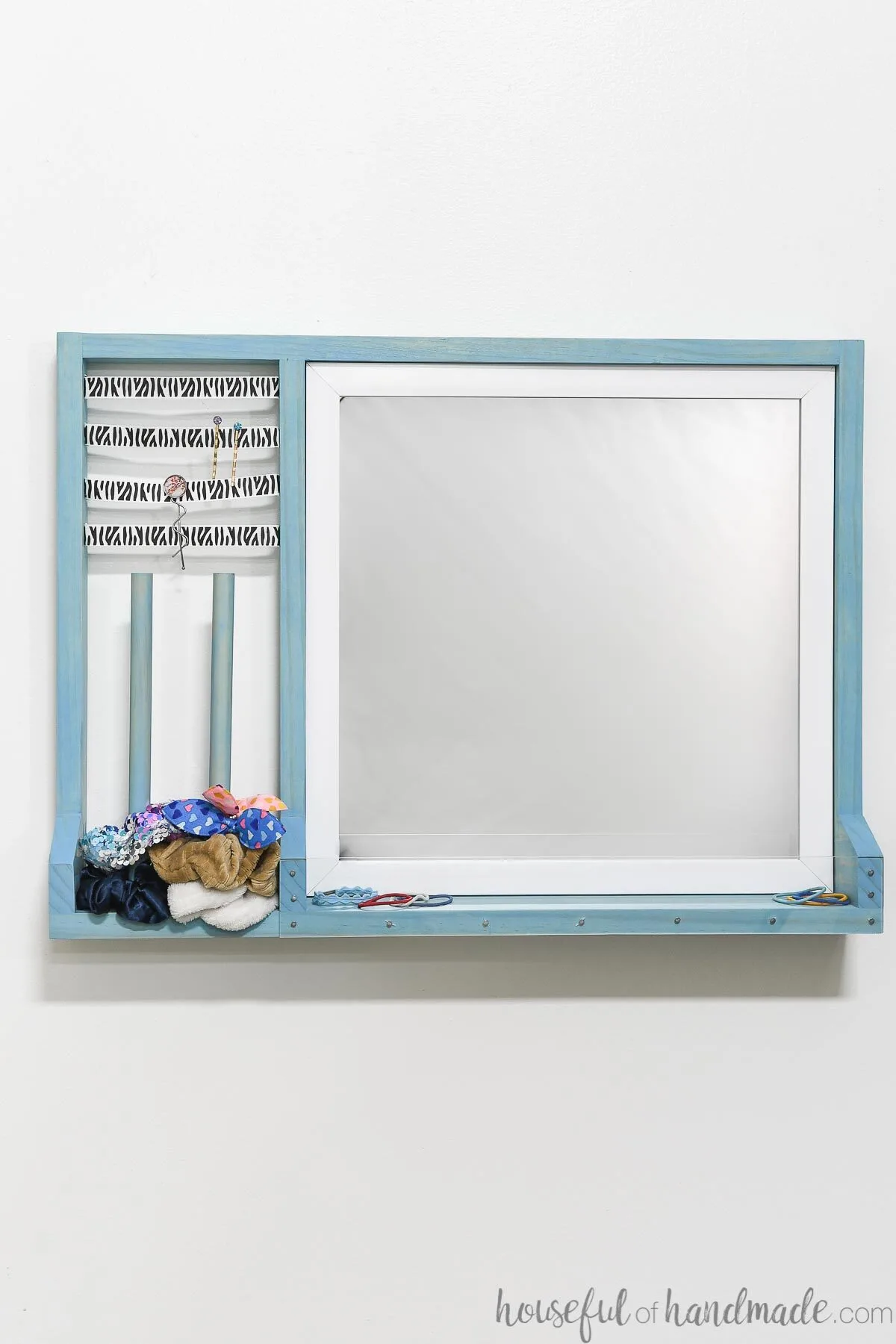 Wall mounted hair accessory organizer with a mirror and storage for scrunchies, hair clips and hair ties. 