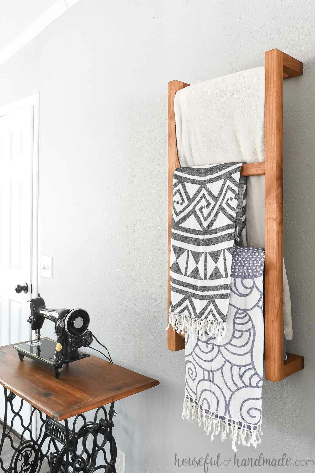 Side view of the wall mounted ladder hanging next to a vintage sewing table with blankets on it. 