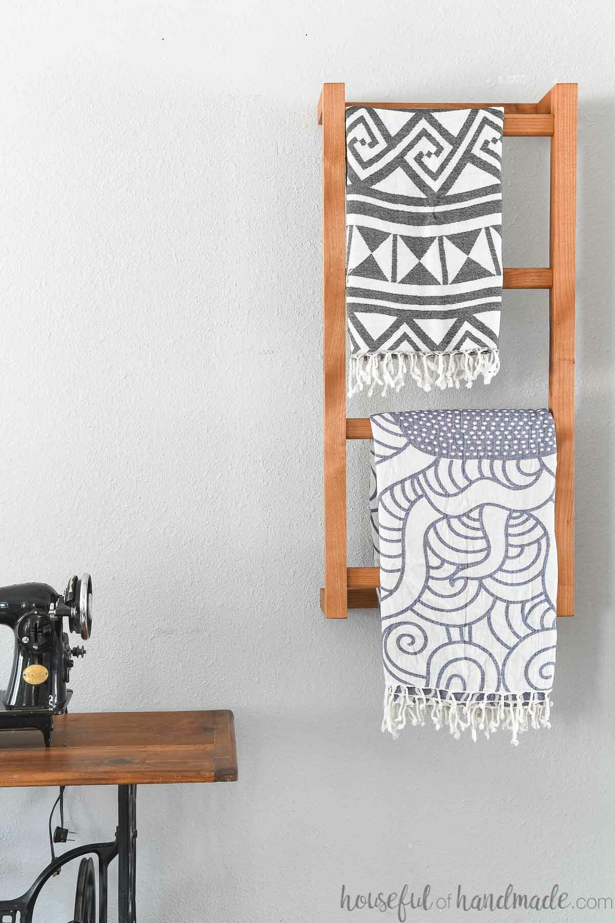 Wall mounted blanket ladder made from wood with two throw blankets on it. 