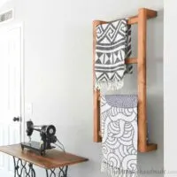 Wall mounted ladder hanging on a bedroom wall with 2 woven throw blankets hanging on it.