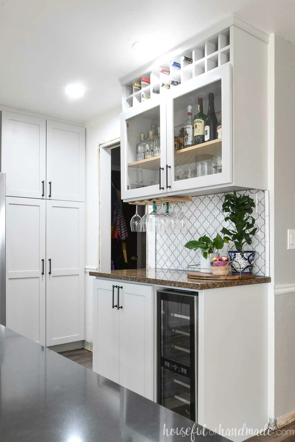 Side wall in the modern kitchen turned into a dry bar with built in wine fridge and glass door upper shelves with wine bottle storage.