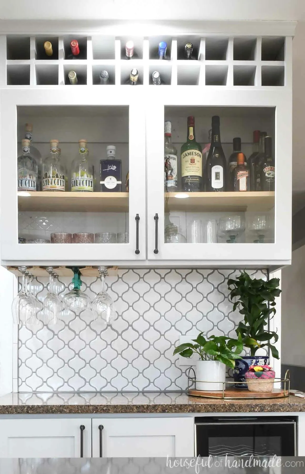 Dry bar cabinet with glass panel doors and square cubbies on top to hold wine bottles.