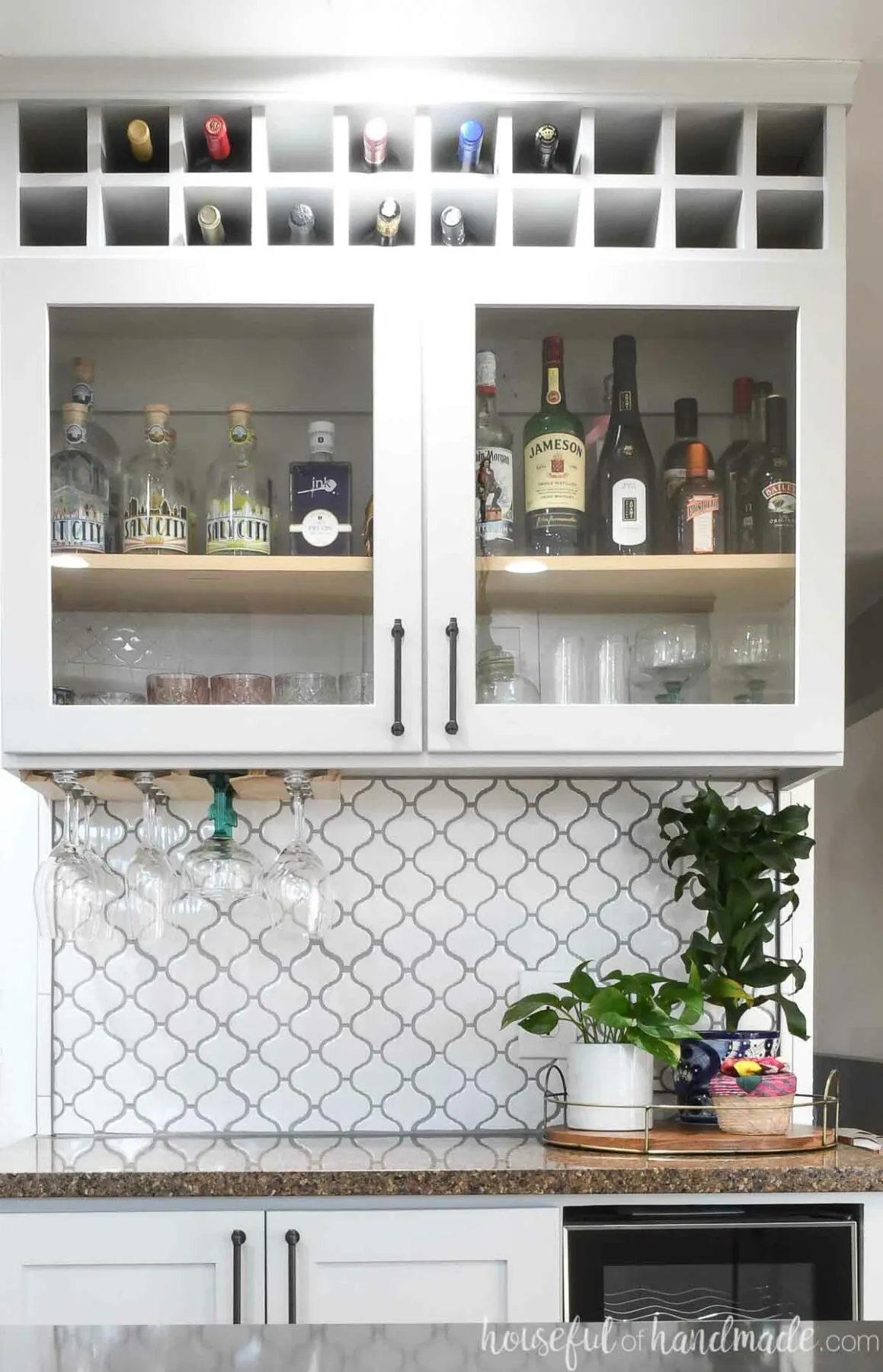 Dry bar cabinet with glass panel doors and square cubbies on top to hold wine bottles. 