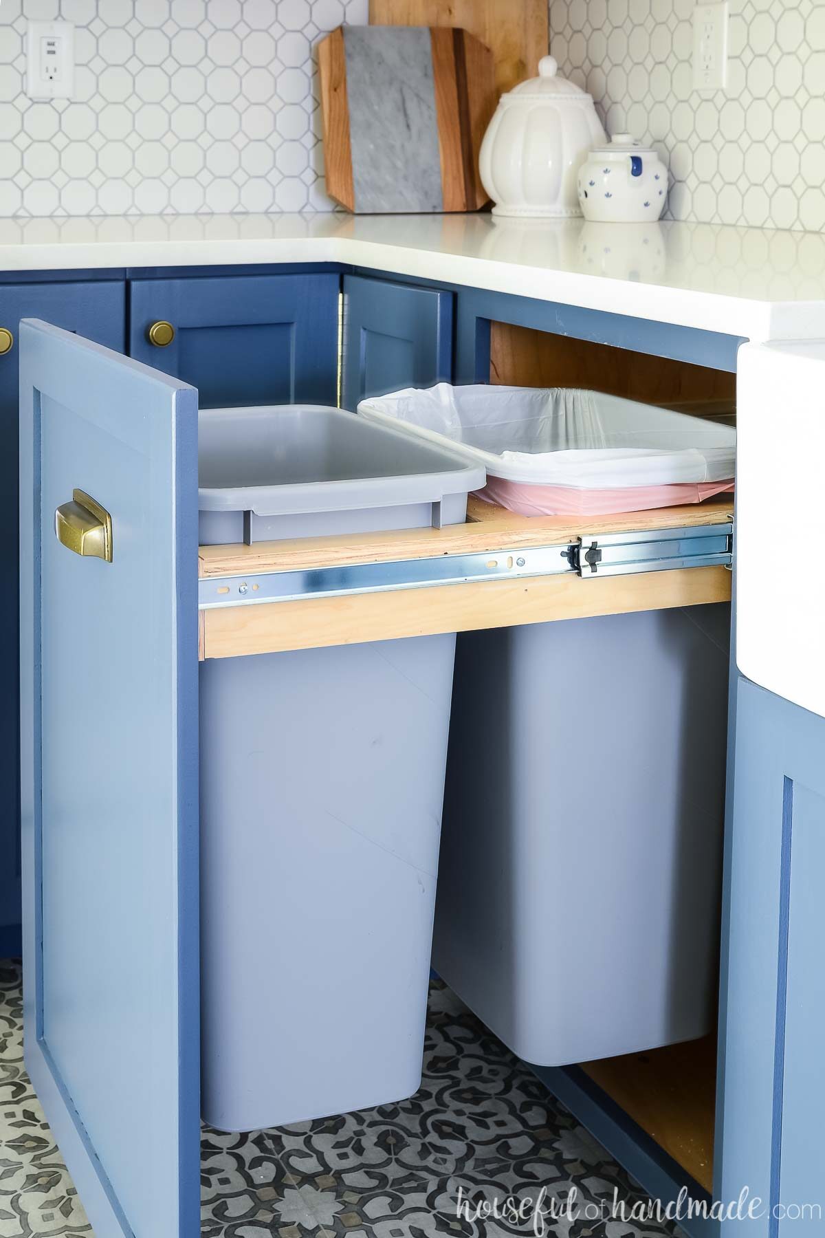 Blue kitchen cabinets with a pull out trash can cabinet holding two full size kitchen garbage cans. 
