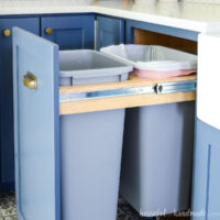 Pull out trash can cabinet slide open revealing the two large garbage cans inside.