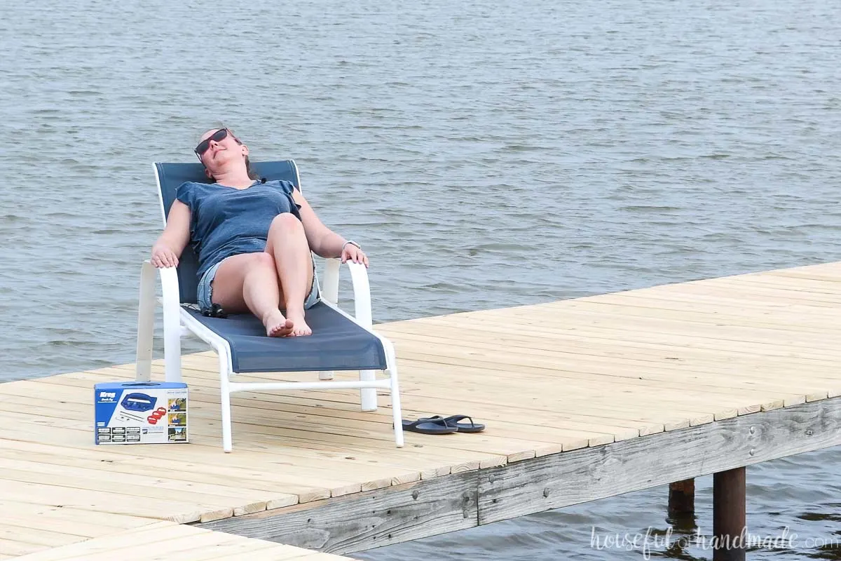 Girl lounging on a  white and blue lounge chair on a deck with new deck boards overlooking the lake. 