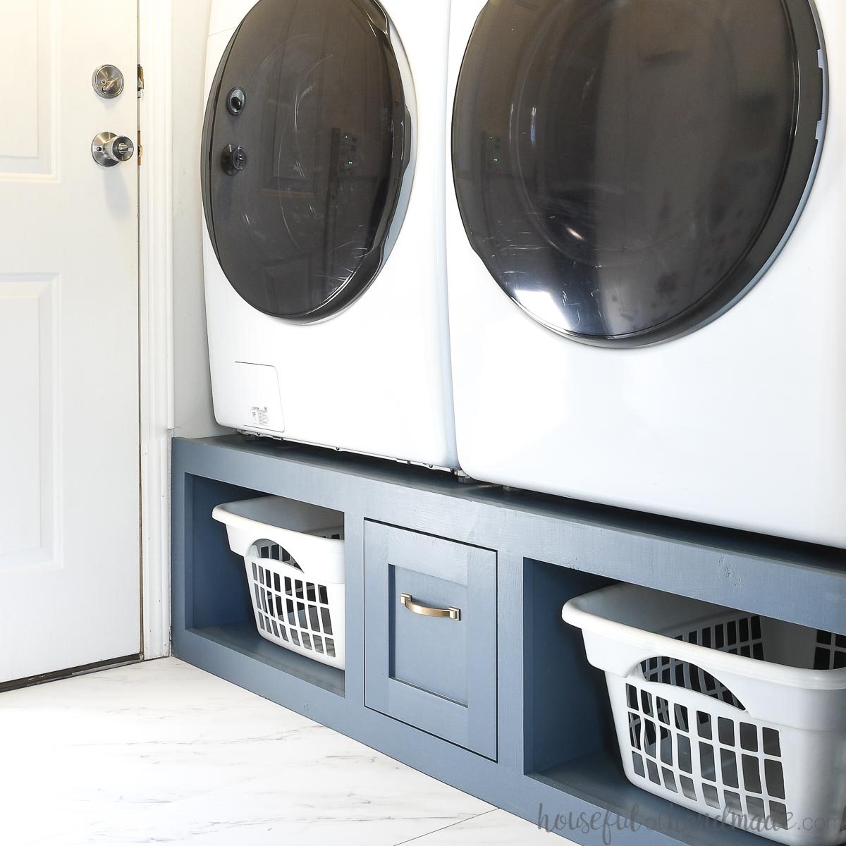 Navy blue washer dryer platform with a drawer in the center of two shelves to hold laundry baskets.