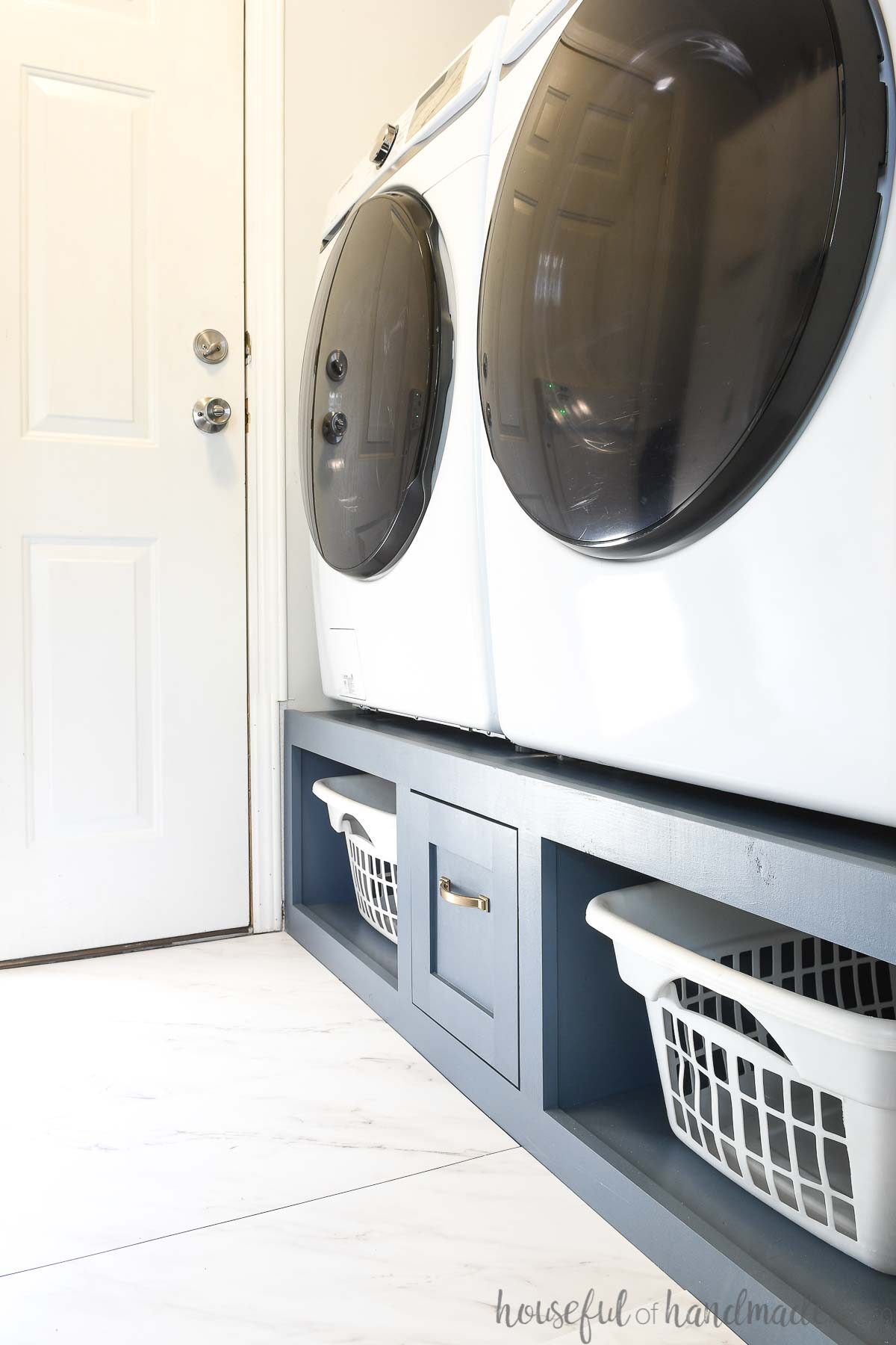 White washer and dryer on a blue painted DIY platform with storage. 