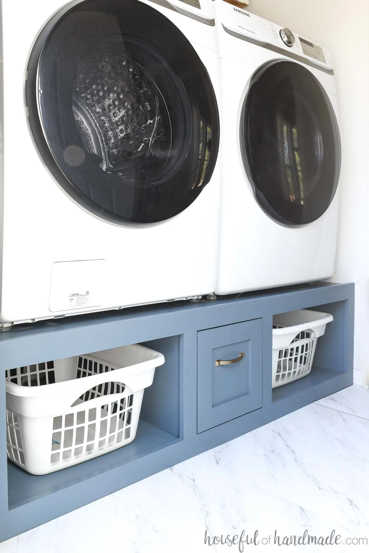 Laundry room with washer and dryer sitting on a blue painted platform with laundry basket shelves and a drawer. 