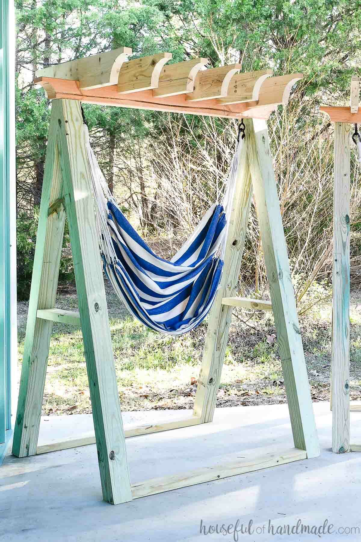 Hanging chair with stand that is an A-frame made of 4x4 posts with a pergola top for shade. 