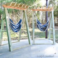Two hammock chair stands with blue and white stripped hammocks hanging in them on a porch.