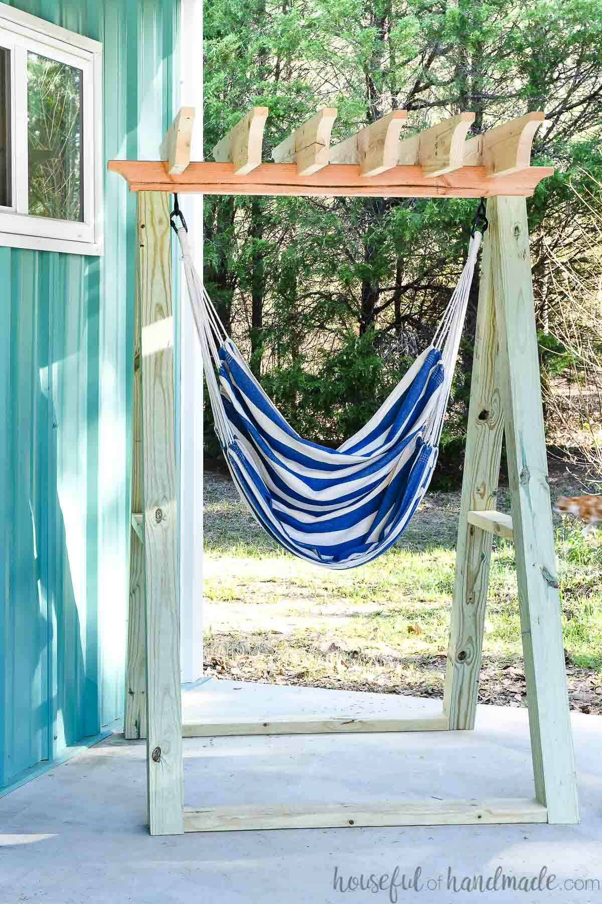 Blue and white striped fabric hammock chair in a wood hanging chair stand on a porch. 
