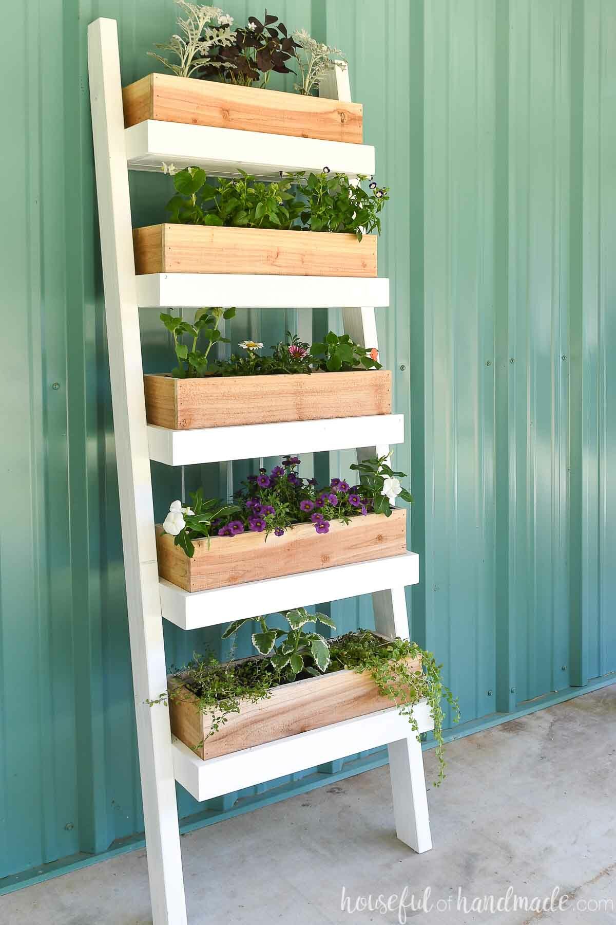 Five tiered ladder planter with plants and herbs planted in it up against a metal building. 