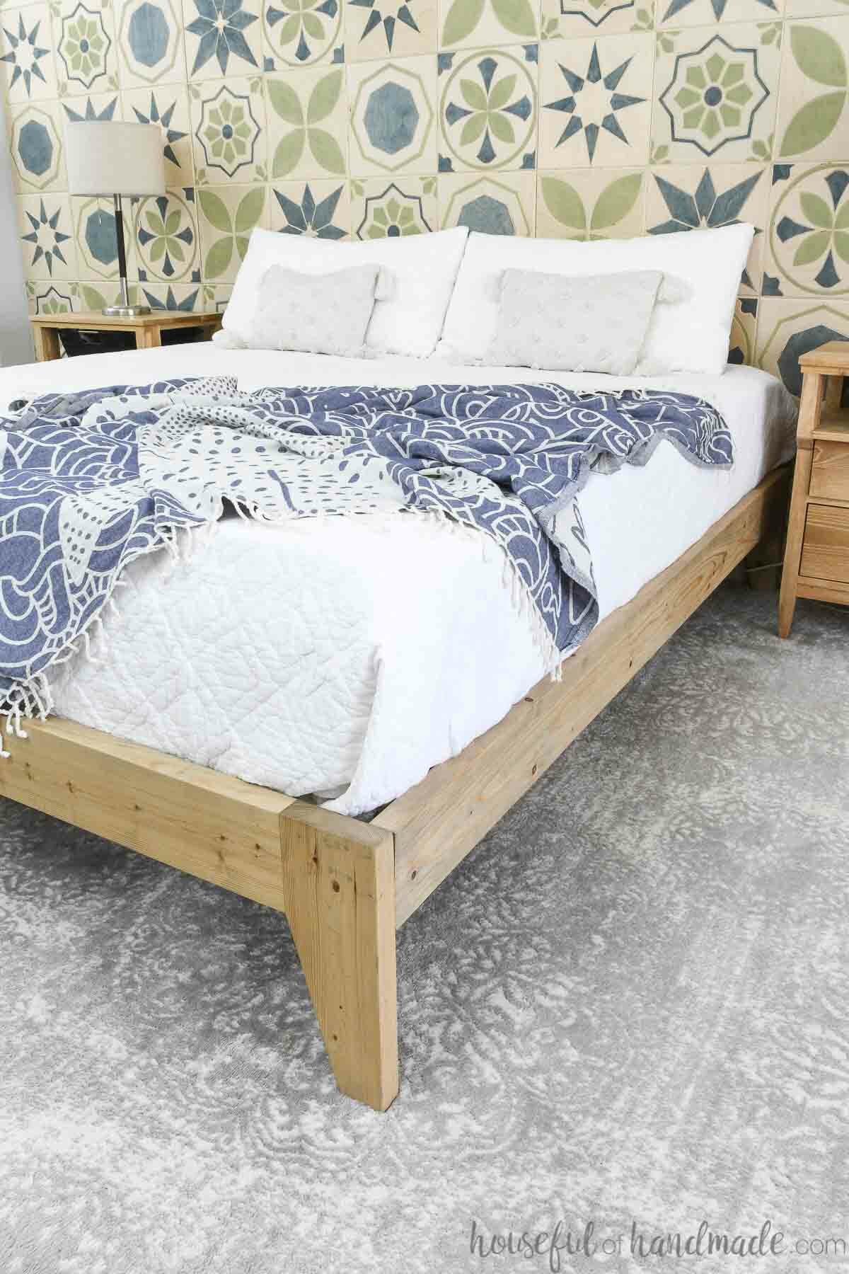Bed on a wood bed frame with tapered legs covered in a white blanket. 