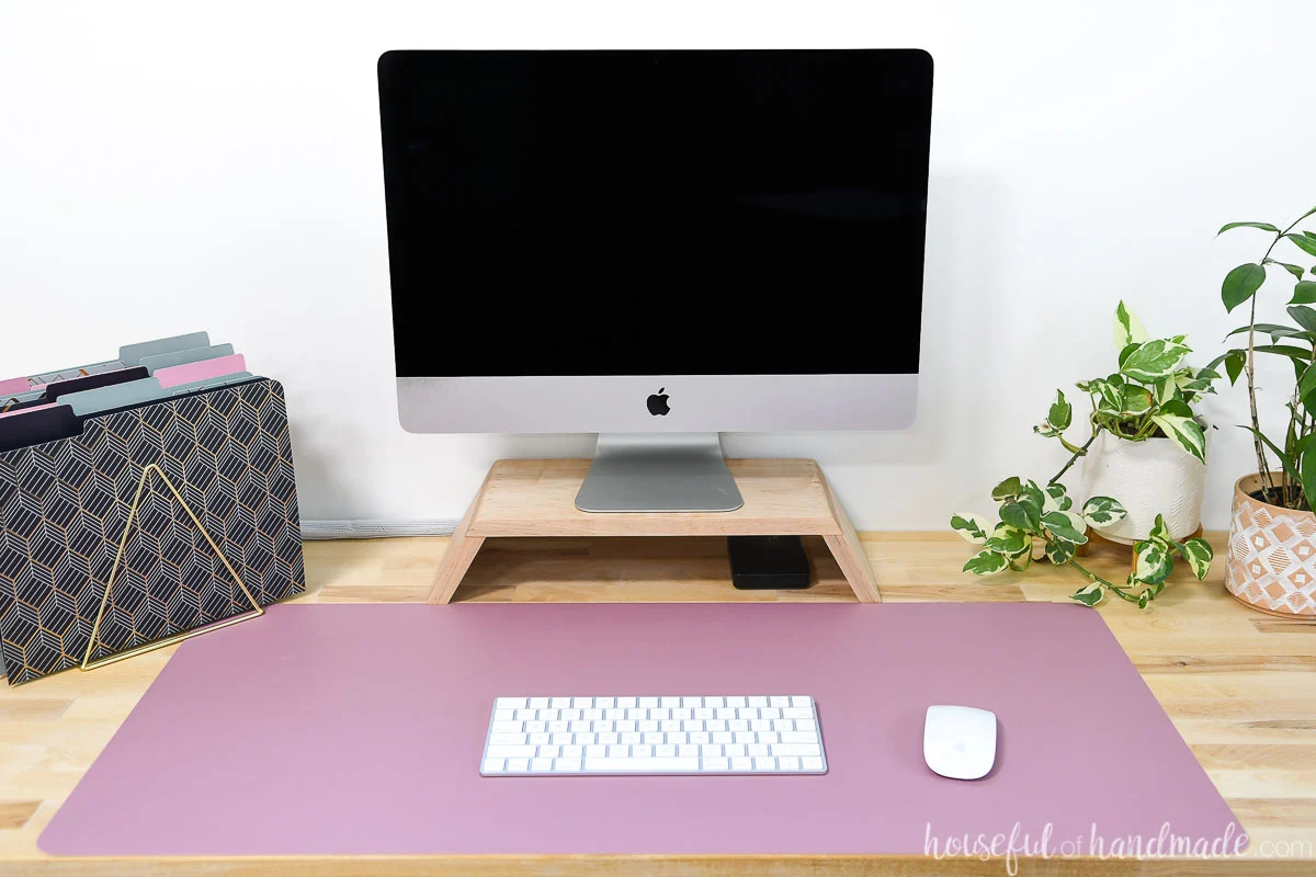 DIY monitor riser on a butcher block desk with pink desk mat.