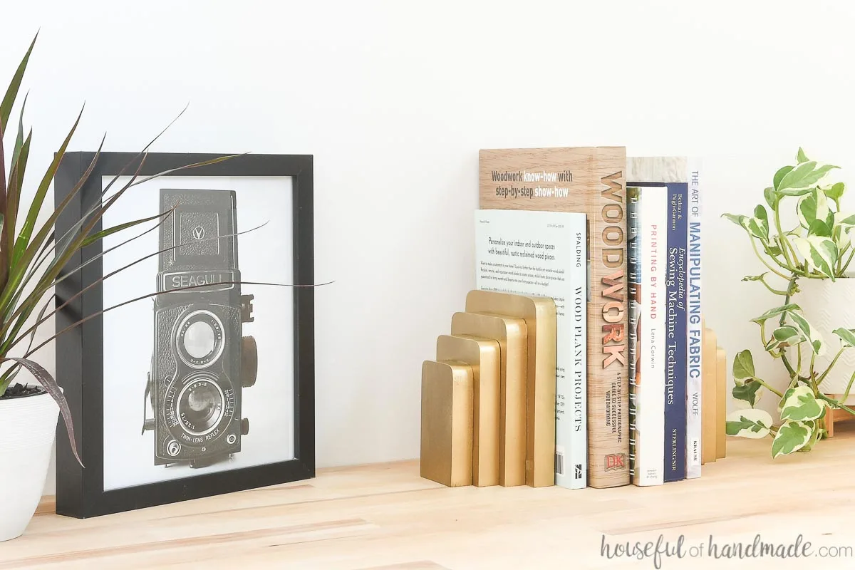 Stack of books displayed next to a photo and plants with handmade bookends from wood scraps. 