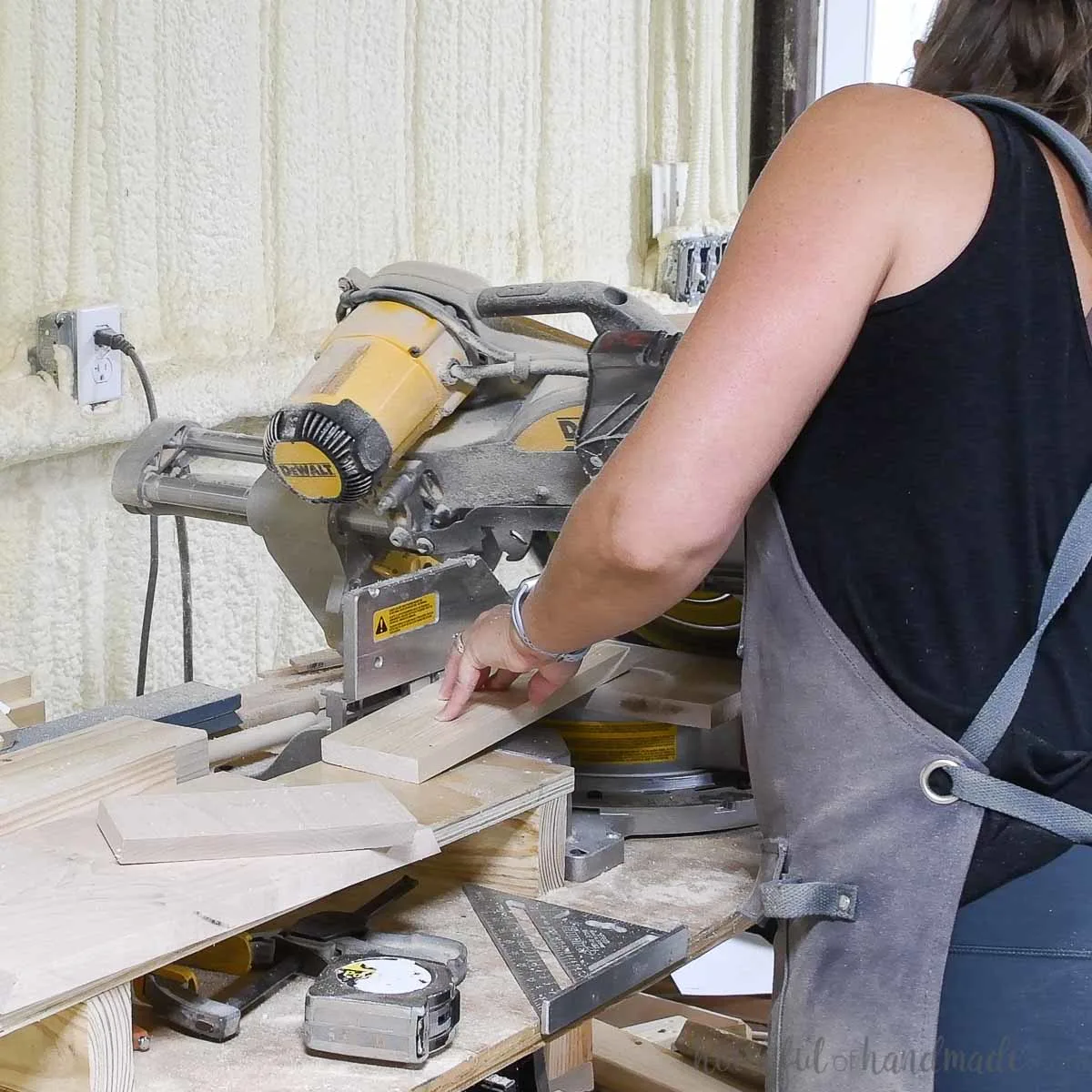 Cutting the legs of the monitor riser with the miter saw using a scrap piece of wood to keep fingers away from the blade. 