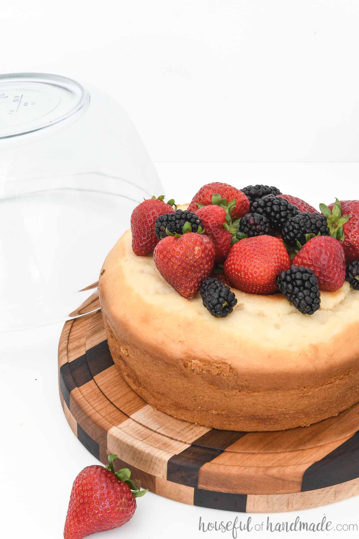 DIY cake plate with glass dome sitting off the side showing the cake covered with berries.