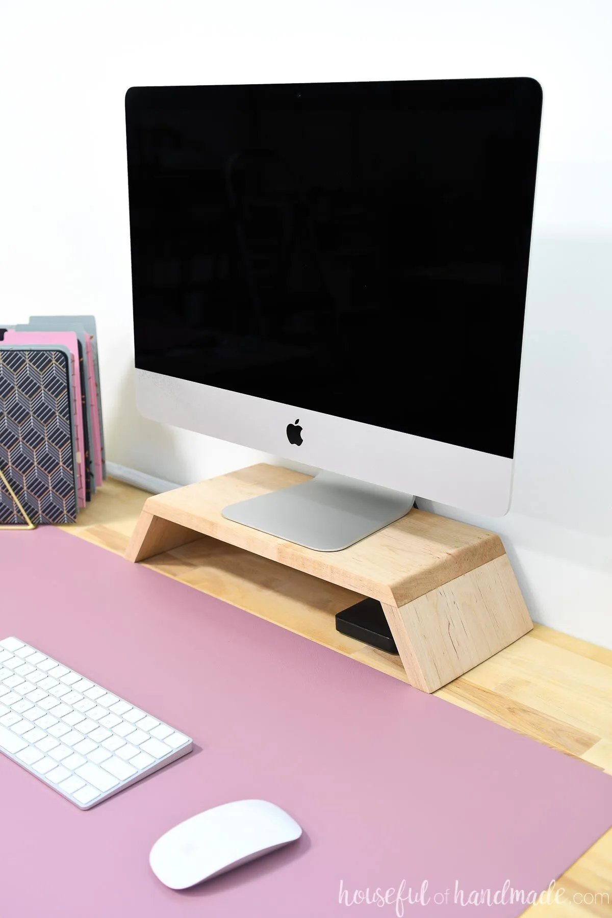 Looking down on a computer desk with pink desk mat and iMac on a DIY monitor stand. 