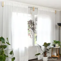 Room full of plants and white sheer curtains hung with DIY scrap wood curtain rod brackets.