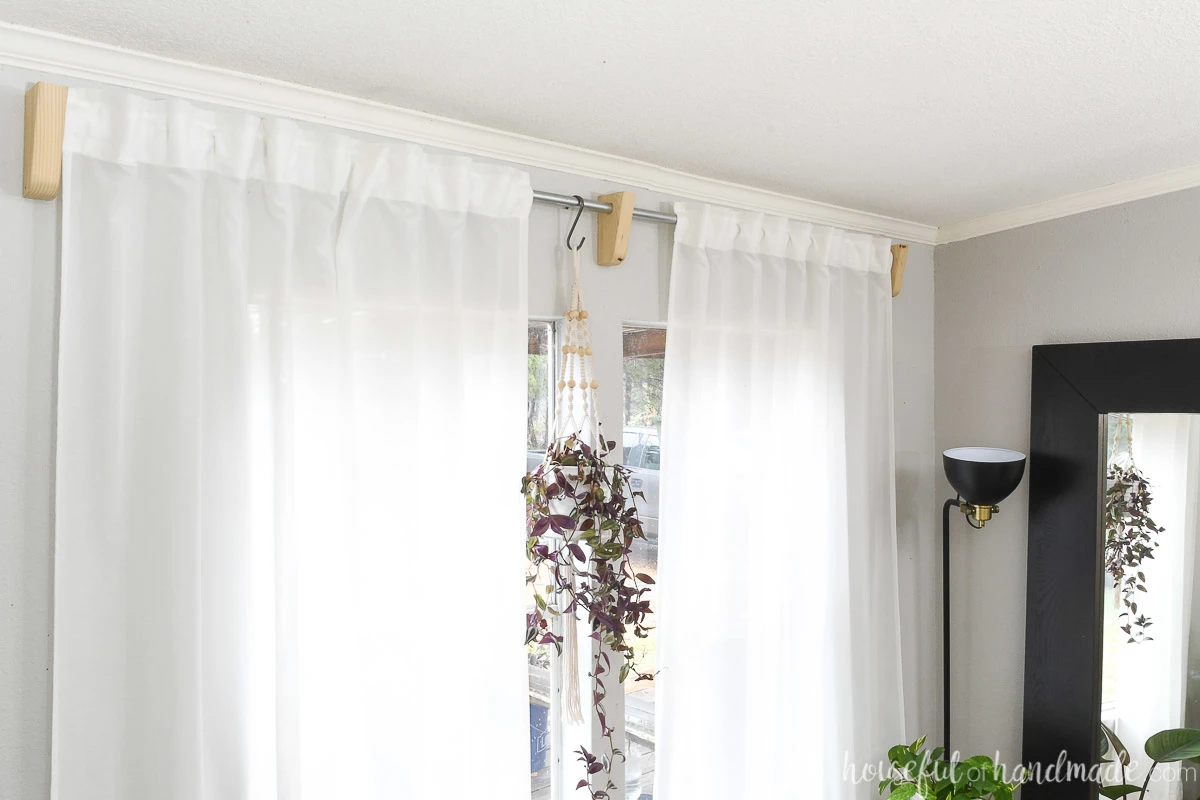 Room with white curtains held up with wood curtain rod brackets made from scrap wood. 