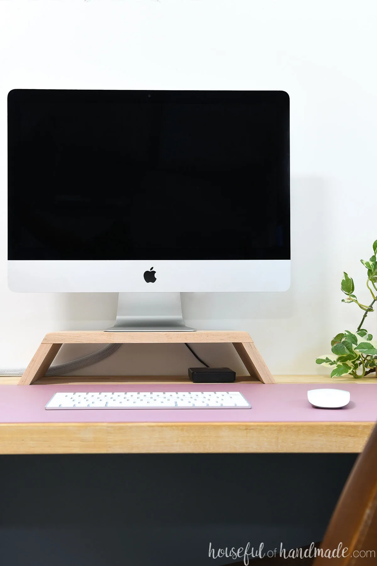 Homemade monitor stand made from wood on a desk with a computer on top next to a plant. 