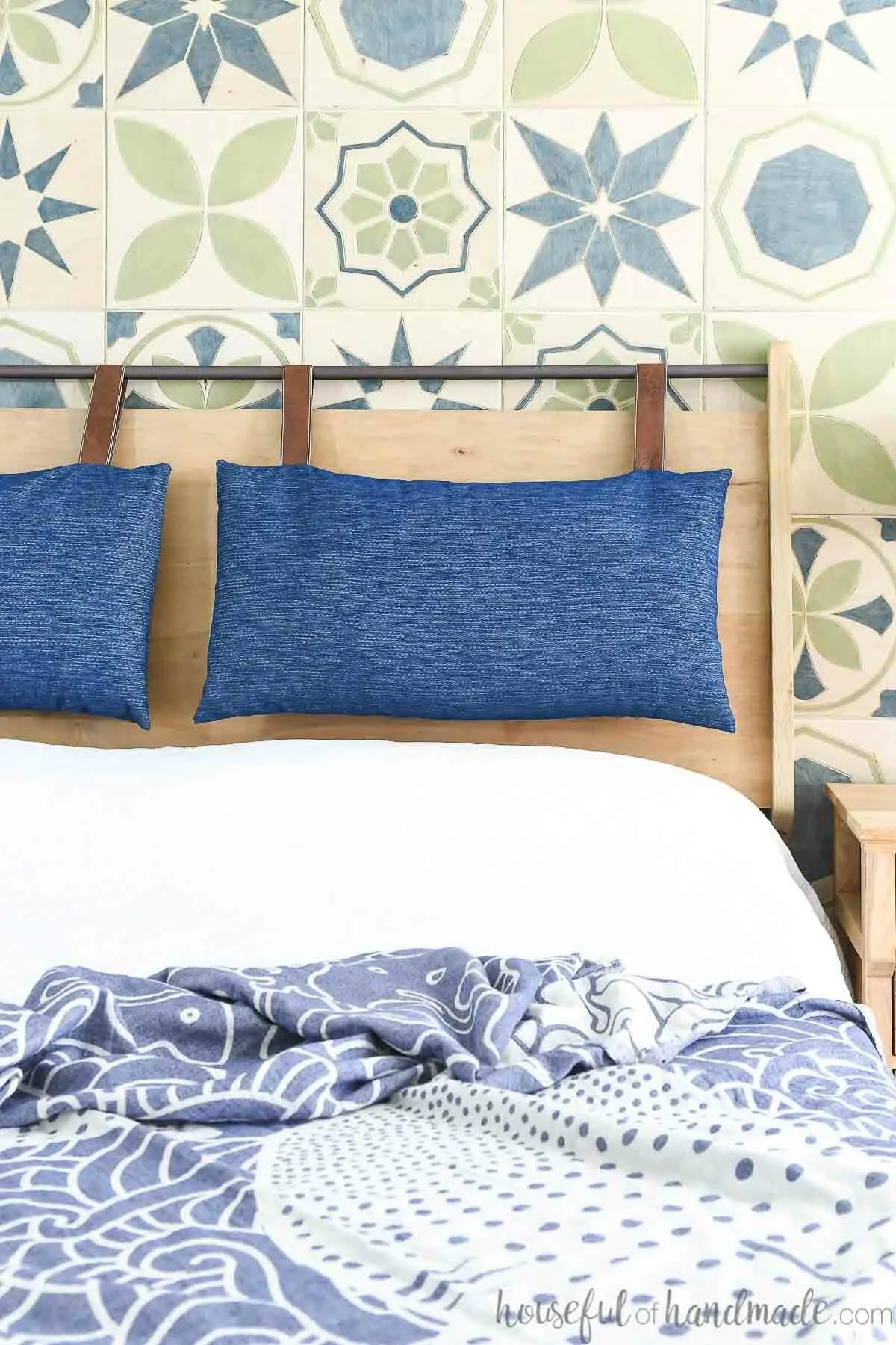 DIY wood headboard with metal bar on top holding two navy and leather headboard cushions.