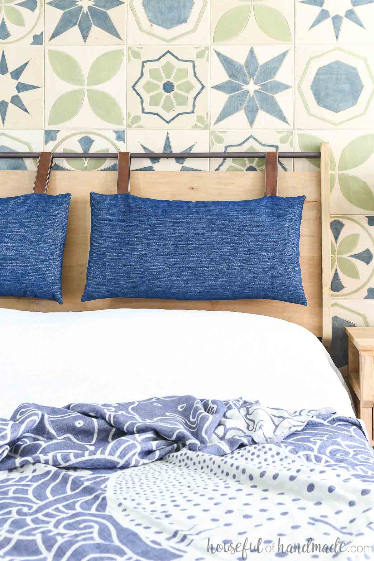 DIY wood headboard with metal bar on top holding two navy and leather headboard cushions. 