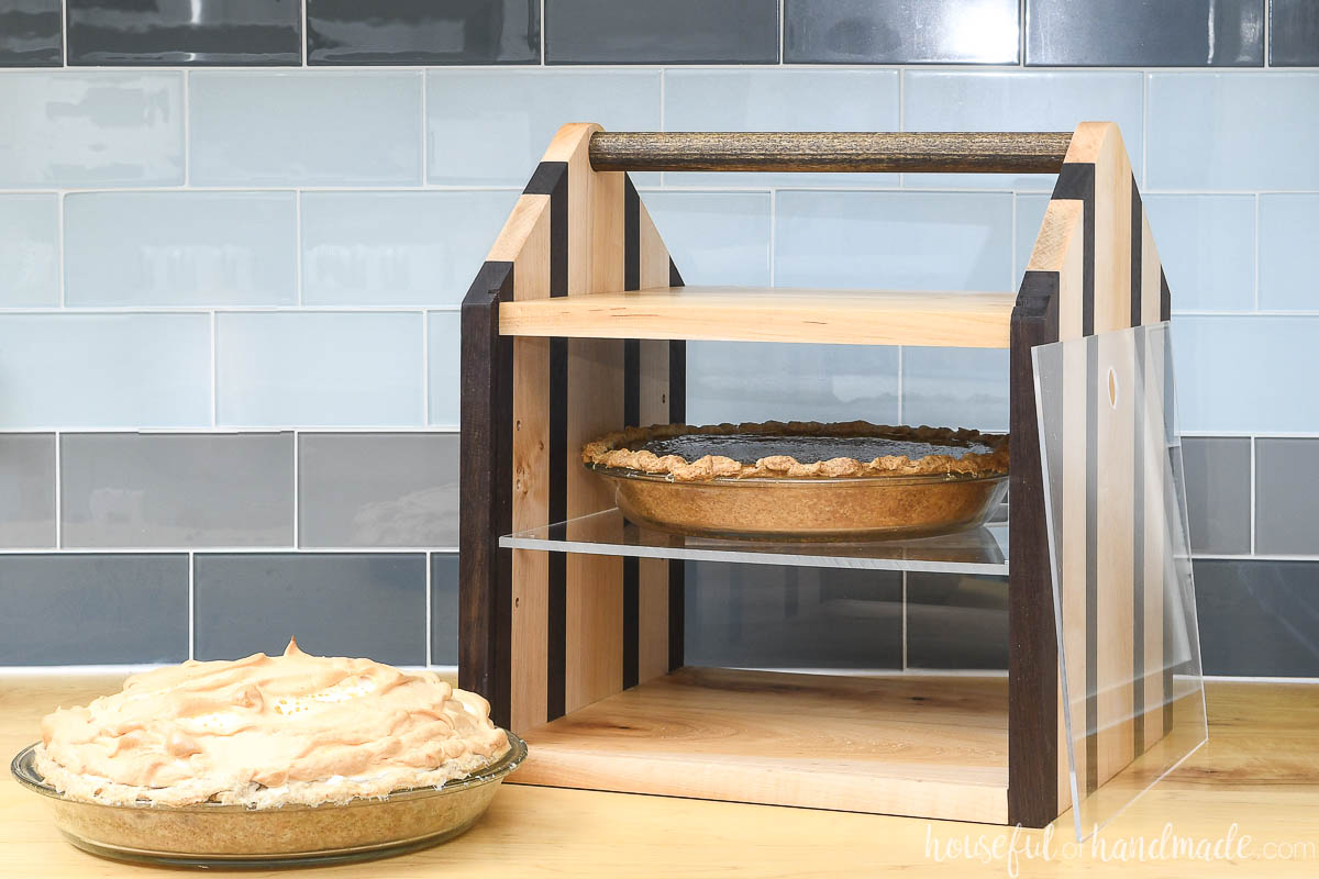 Two pie wooden pie carrier with an acrylic shelf and handle on a countertop. 