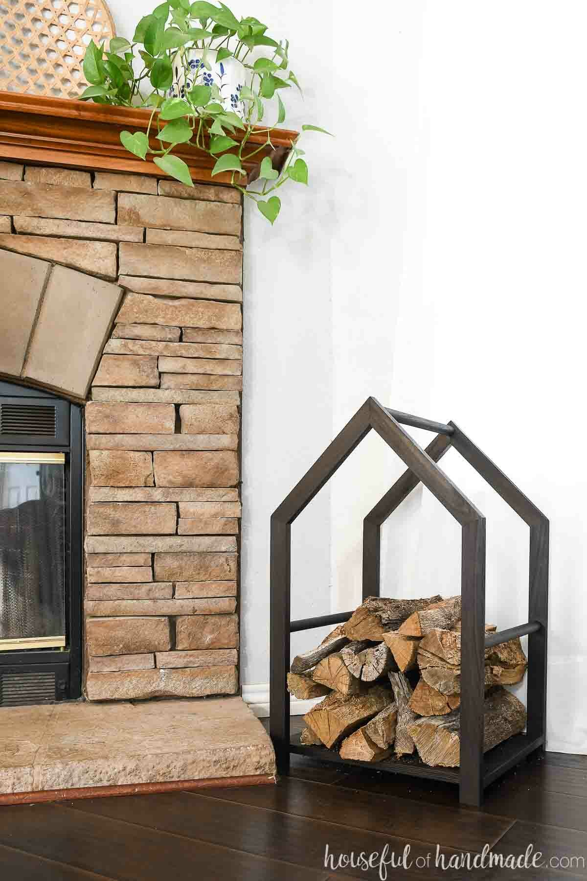 Black house shaped log holder next to a fireplace with firewood in it. 