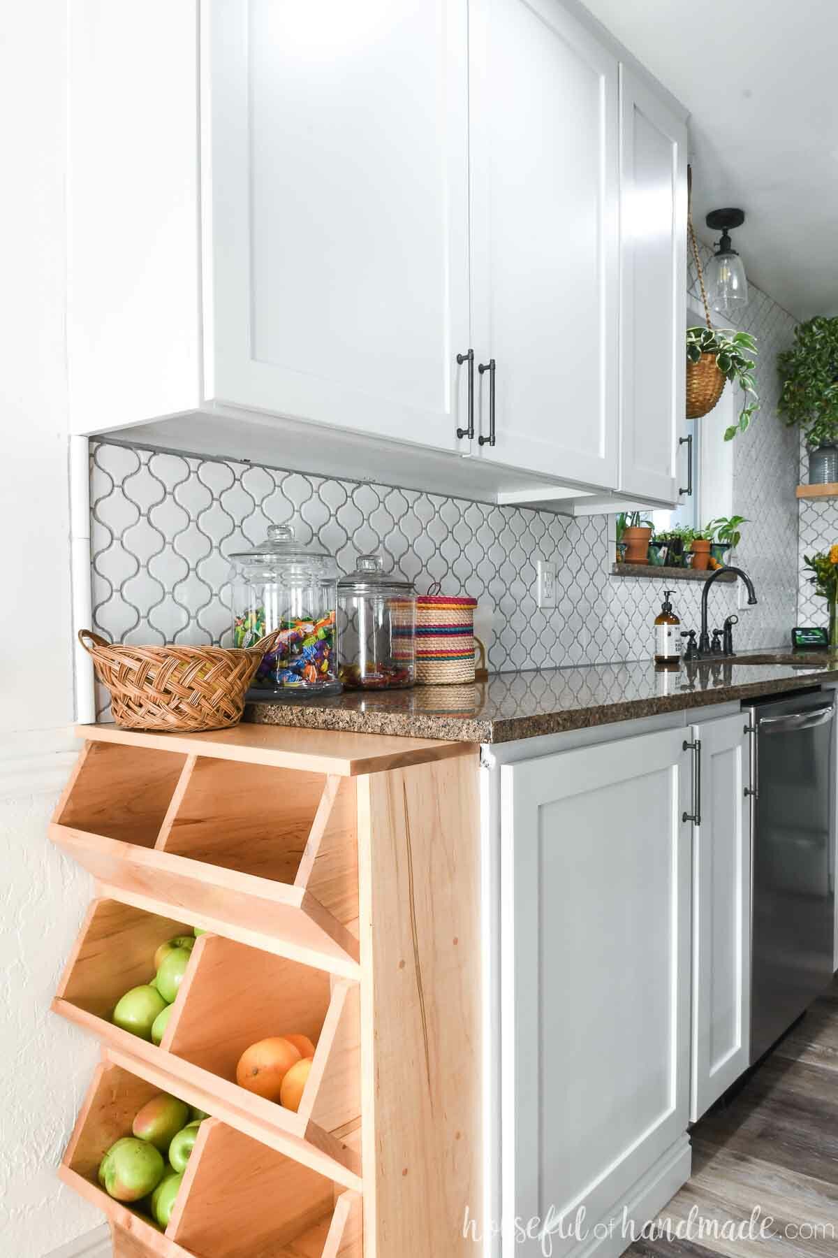 Kitchen with wooden produce bins on the end of the base cabinets filled with fruits and vegetables. 