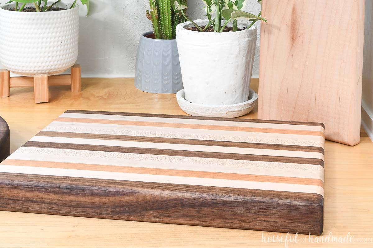 DIY 1 1/2" thick cutting board sitting on a wood countertop in front of plants. 