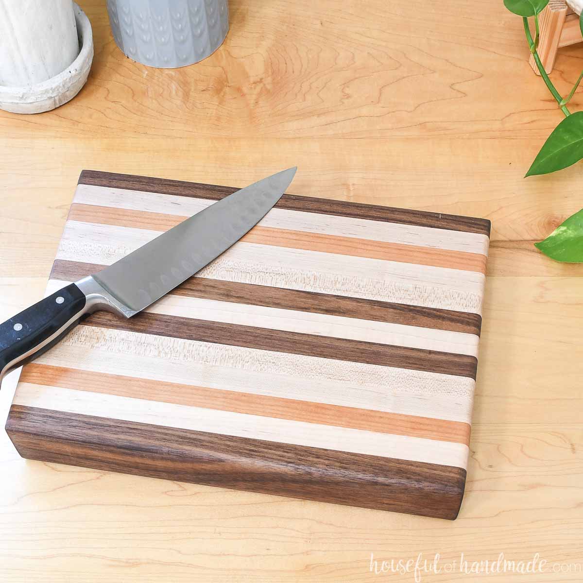 10x14 edge grain cutting board made from walnut, cherry and maple 1x2 boards with a chef's knife sitting on top of it.