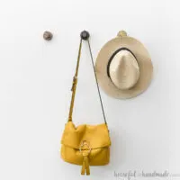 Purse and hat hanging on metallic wood hooks on a white wall.