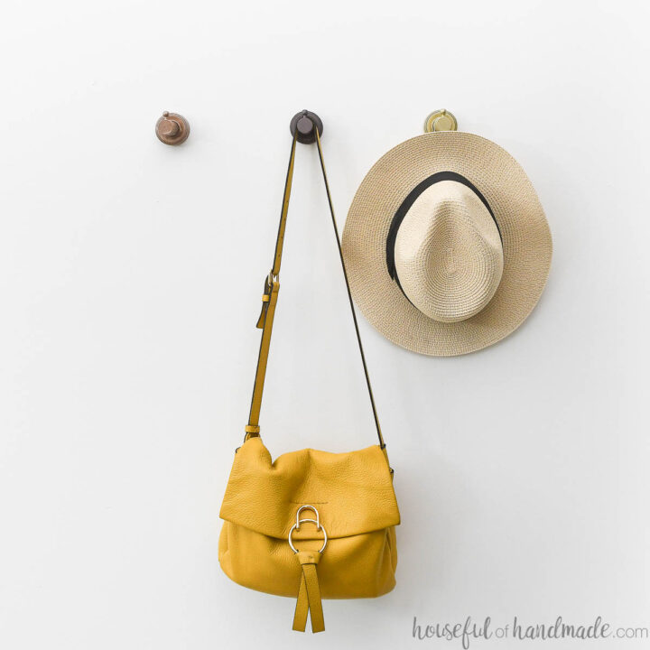 Purse and hat hanging on metallic wood hooks on a white wall.