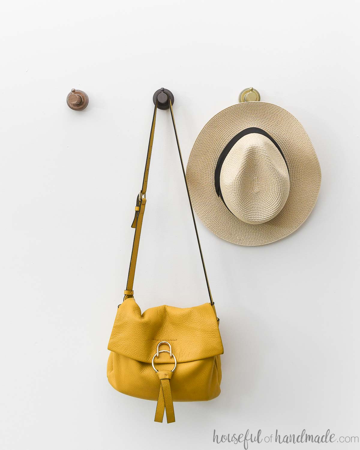 Three metallic painted wood wall hooks on a white wall with a purse and hat hanging on two of them. 