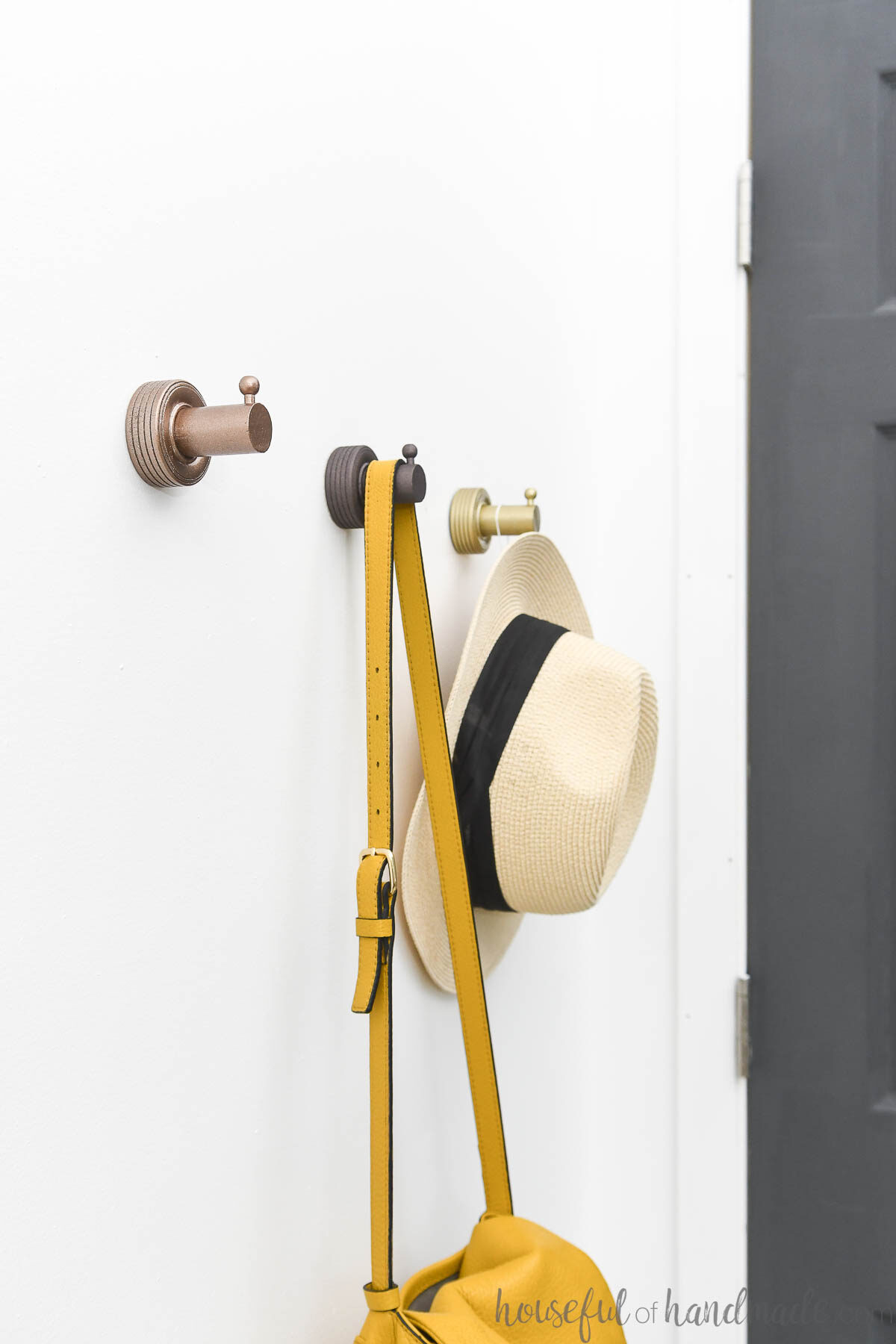 Thee DIY wall hooks made from wood dowels and wood wheels on a wall next to a charcoal painted door. 