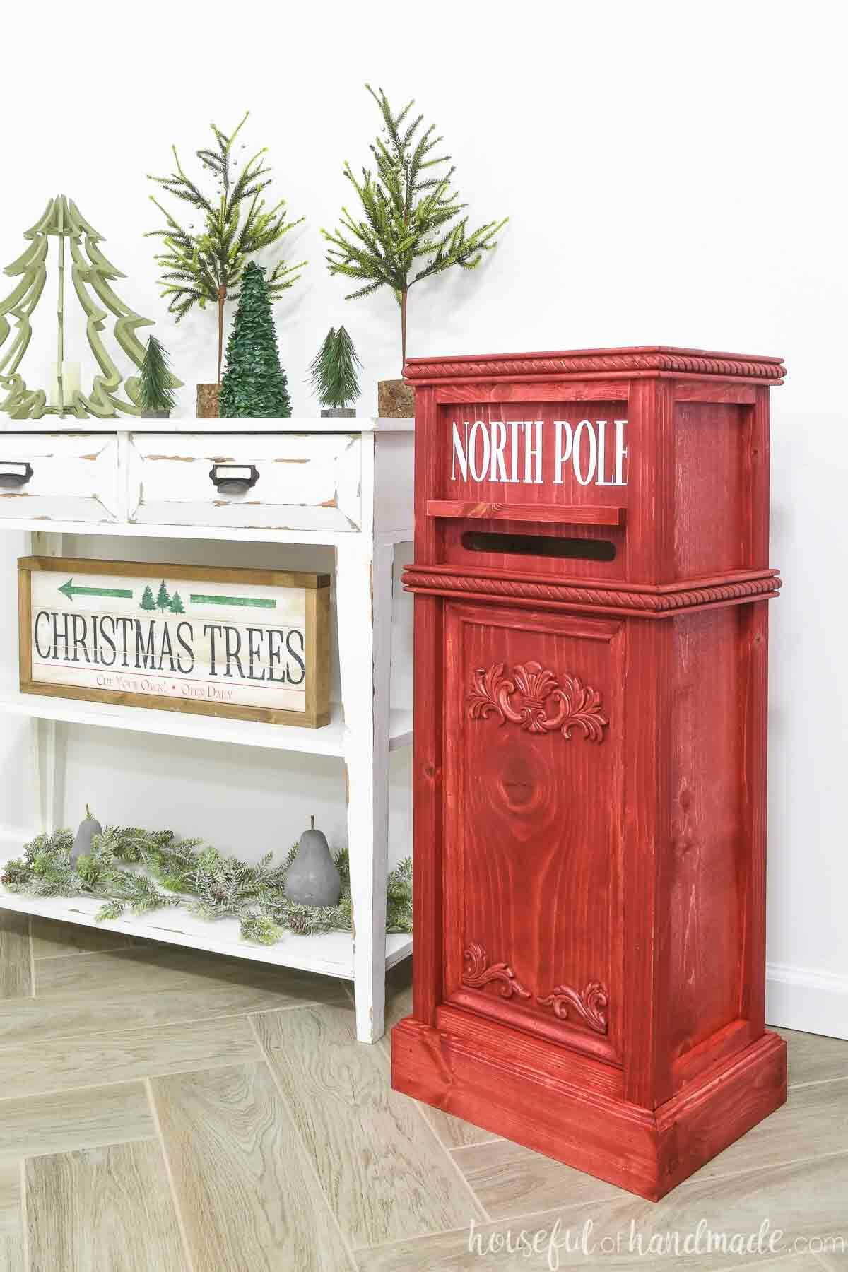 3' tall Santa mailbox sitting next to a console table decorated for Christmas. 