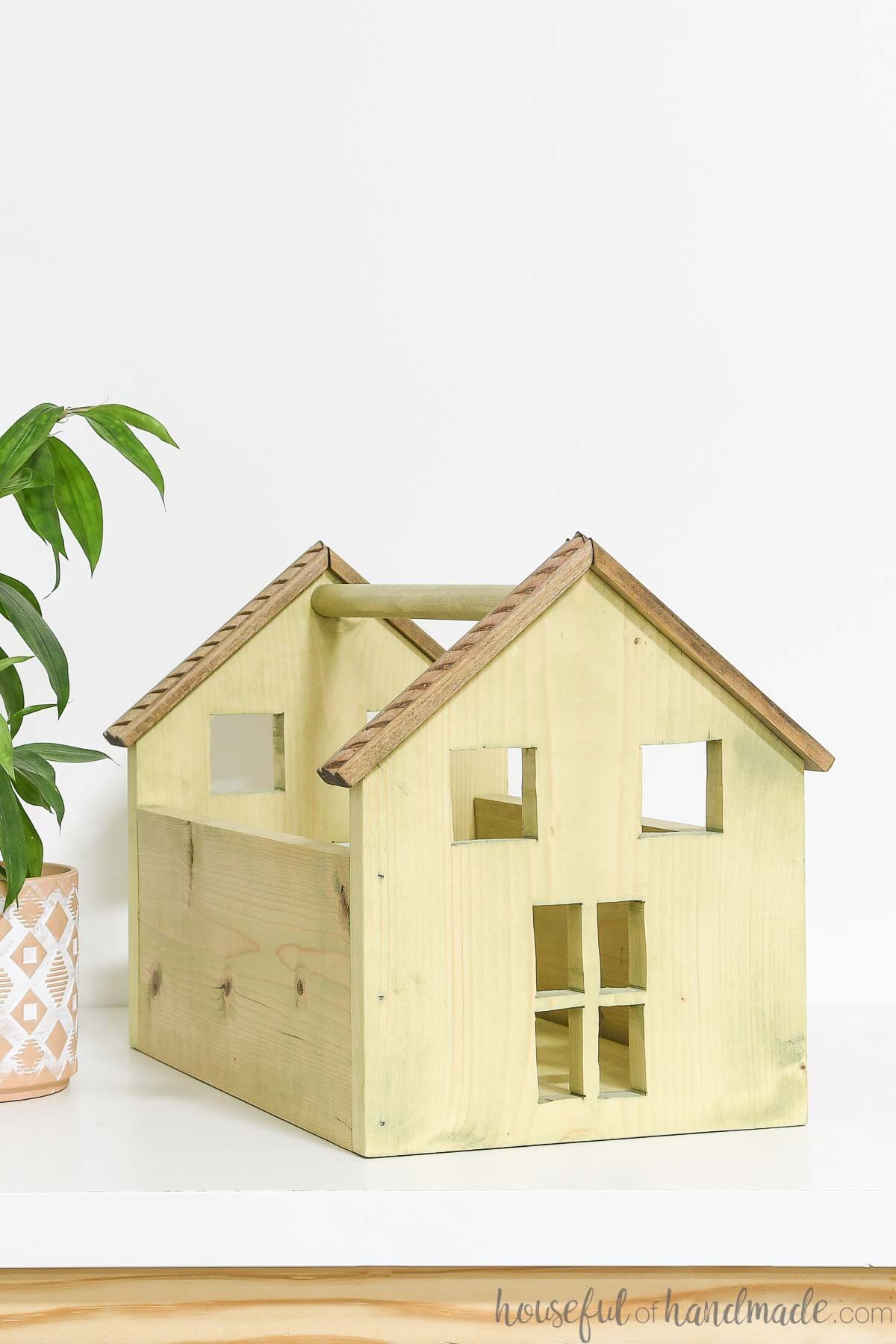 Simple wood dollhouse with a carrying handle and cut outs for doors and windows. 