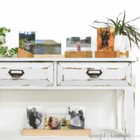 Five different modern picture frame blocks holding pictures between plexiglass sheets on a console table.