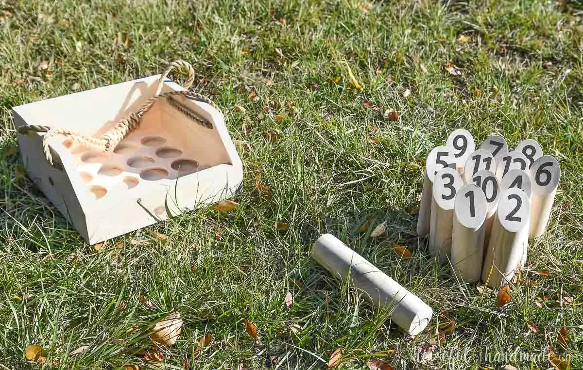 Mölkky game set up in the grass with a carrier to hold all the pins next to it. 