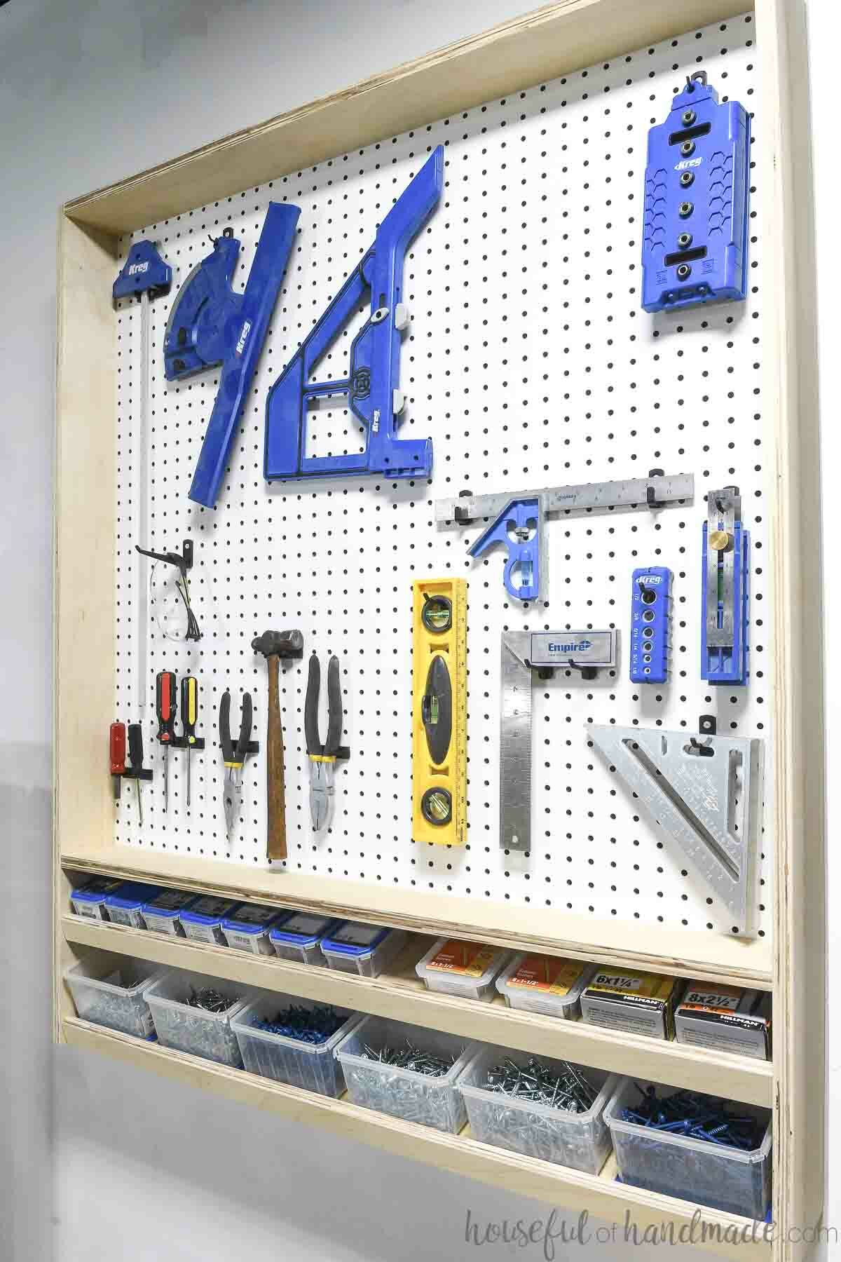 Pegboard wall organizer with plywood frame around the pegboard and angled shelves at the bottom for screw storage. 