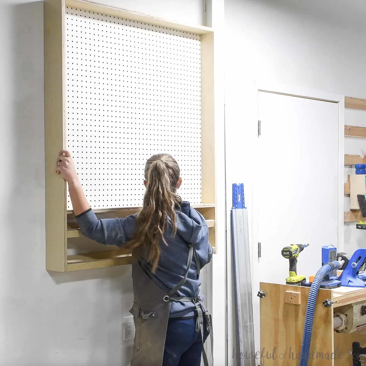 Kati hanging the finished pegboard storage cabinet on the wall 
